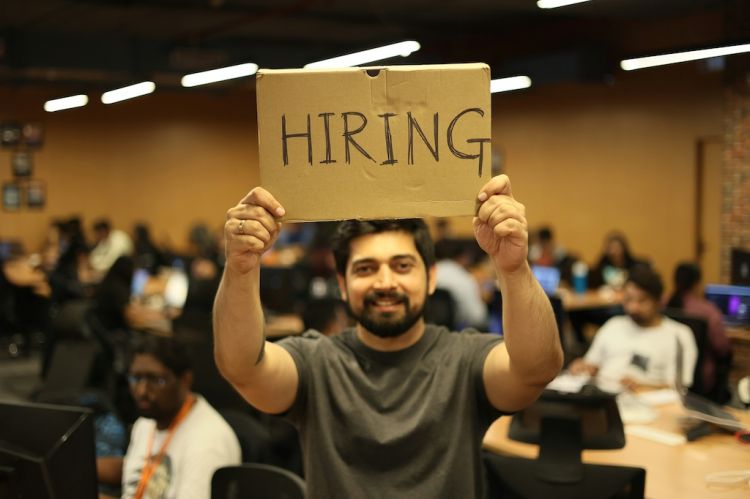 a man holding a cardboard sign that says "hiring"